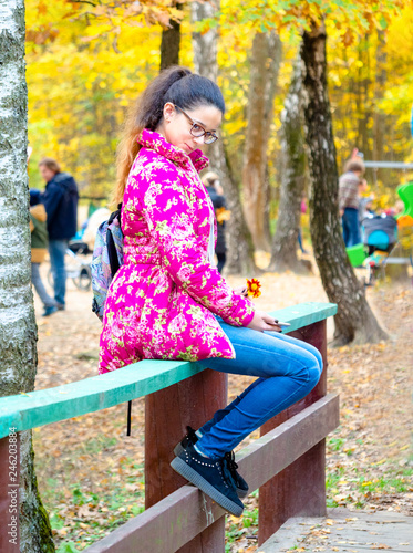 Charming grimacing girl in the autumn forest. Portrait of a teenager sitting on a wooden railing in an autumn park on a sunny day. photo