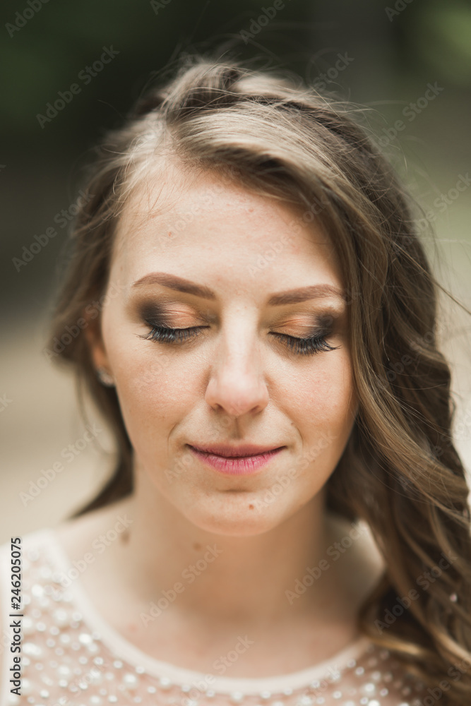 Gorgeous bride in elegant dress holding bouquet posing near forest and lake Gorgeous bride in elegant dress holding bouquet posing near forest and lake
