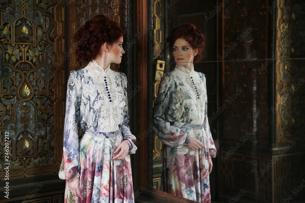 Young beautiful woman standing in the palace room with mirror. Young beautiful woman standing in the palace room with mirror.