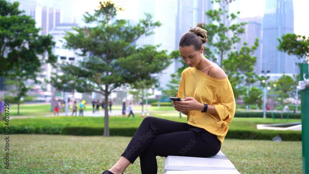 Young beautiful woman texting on smartphone sitting in city park Young beautiful woman texting on smartphone sitting in city park