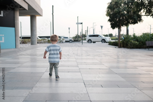 Little booy is walkinbg down the street, view from teh back photo