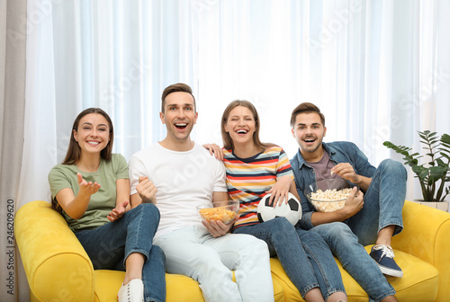 Group of people with snacks and ball watching soccer match on TV at home