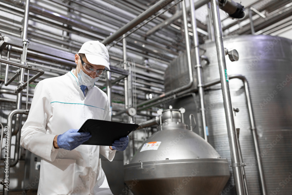 technologist taking necessary notes while standing at production department of dairy factory technologist taking necessary notes while standing at production department of dairy factory