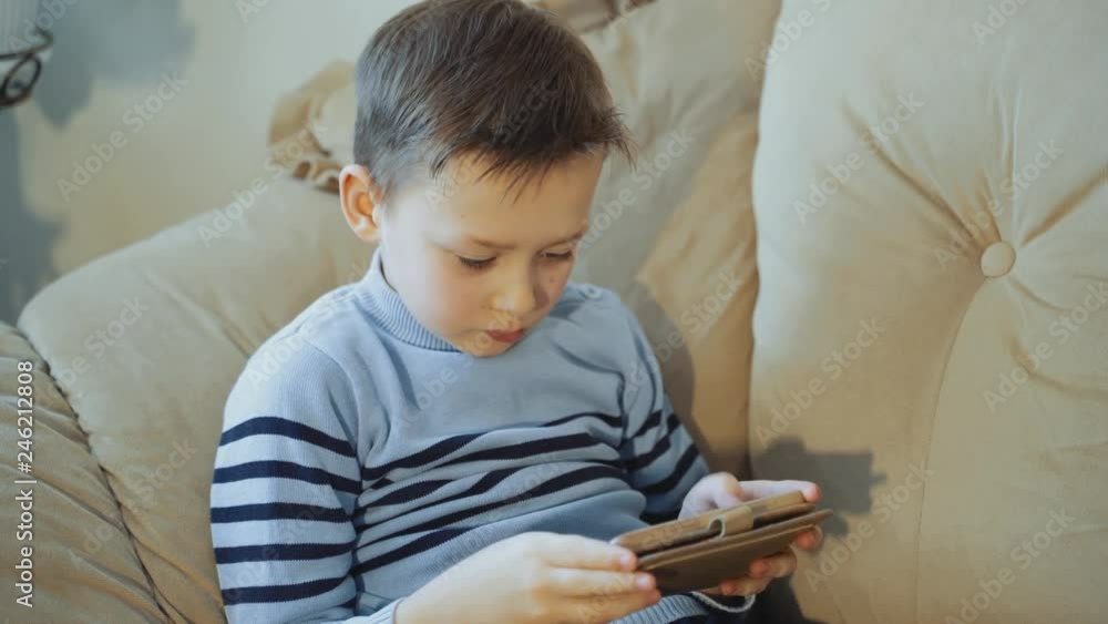 Cheerful pre-teen boy sitting cross-legged on the sofa and playing on his phone. Peaceful pastime. Cheerful pre-teen boy sitting cross-legged on the sofa and playing on his phone. Peaceful pastime.