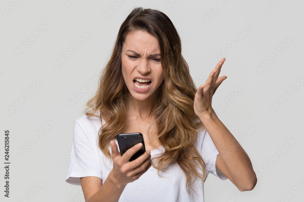 Annoyed angry young woman mad about spam message stuck phone looking at smartphone isolated on blank studio background, furious teen girl having problem with cellphone irritated by broken mobile Annoyed angry young woman mad about spam message stuck phone looking at smartphone isolated on blank studio background, furious teen girl having problem with cellphone irritated by broken mobile