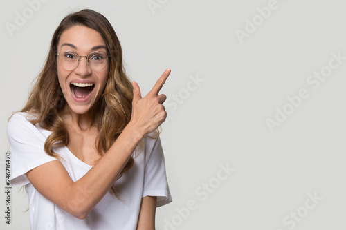 Excited amazed young woman customer pointing finger at copy space aside look at camera, euphoric surprised girl student in glasses advertise sale scream with joy isolated on white studio background photo