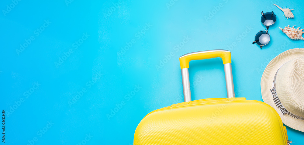 Flat lay yellow suitcase with sunglasses and a hat on a blue background. The concept of travel, rest and relaxation. Banner