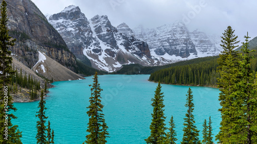Moraine Lake - A panoramic view of Moraine Lake and its surrounding mountains on a snowy and foggy Spring day, Banff National Park, Alberta, Canada.