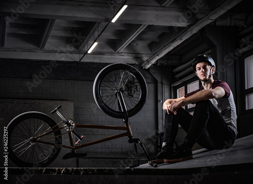 Young Bmx rider relaxing after practicing tricks with his bike in a skatepark indoors