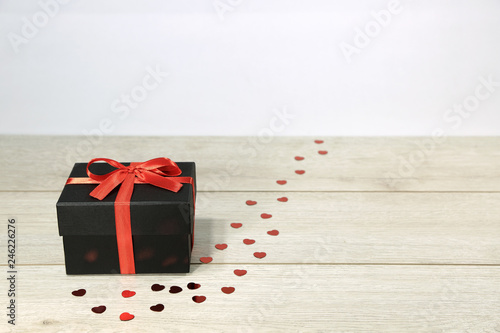 Czarne pudełko z czerwoną wstążką i sercami na deskach.