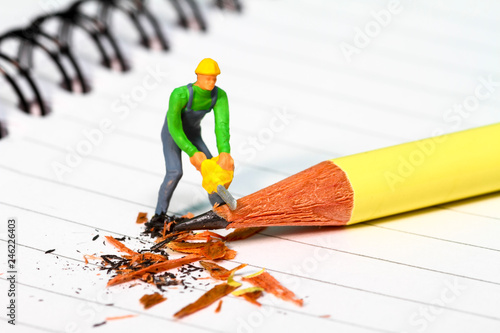 Conceptual diorama image of a miniature figure sharpening a pencil on a note book photo