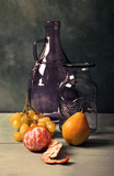 Still life with blue glass vase, lilac glass jar and fruit on turquoise background