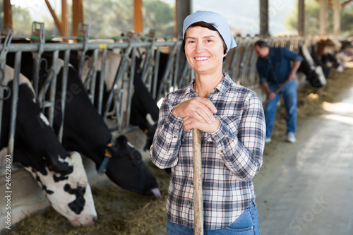 Portrait of smiling female farmer who is standing at her workplace near cows at the farm
