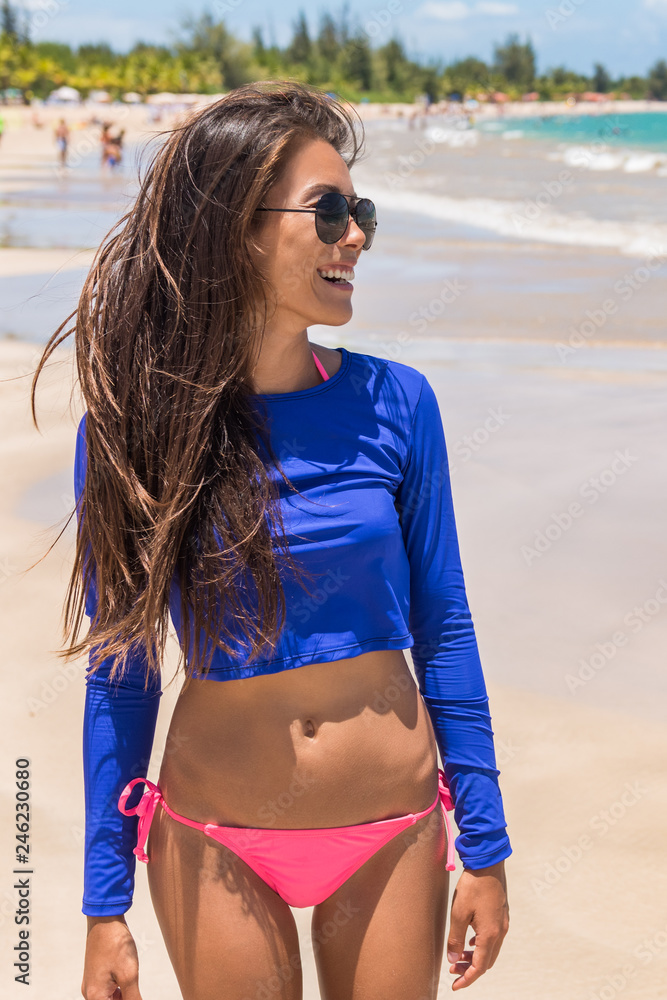 Beach rashguard bikini woman wearing swim shirt rash guard for sun  protection against solar uv rays. Asian girl in sunglasses and beachwear  protective clothing for surf and swimming concept. Stock Photo