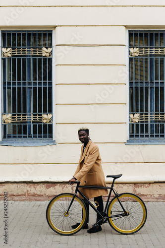 Fototapeta Naklejka Na Ścianę i Meble -  Young handsome businessman walking outdoors with a bicycle. African man going to work on bike on city street.