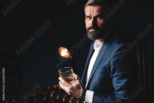 Degustation, tasting. Man with beard holds glass of brandy. Tasting and degustation concept. Bearded businessman in elegant suit with glass of whiskey photo