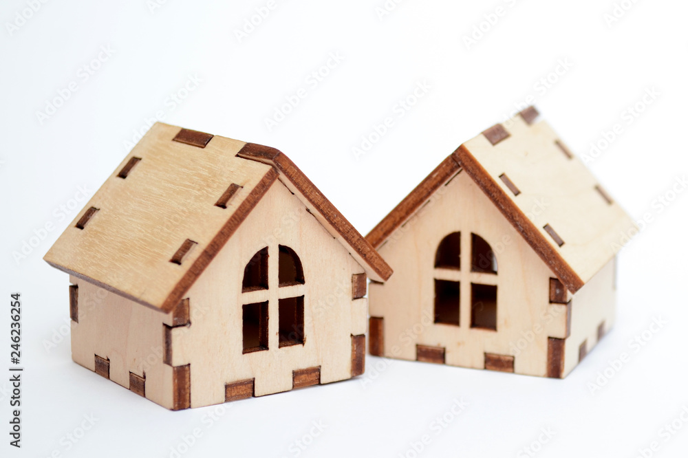 Two wooden toy houses on white background, one house stands behind the other, concept for selling houses Two wooden toy houses on white background, one house stands behind the other, concept for selling houses