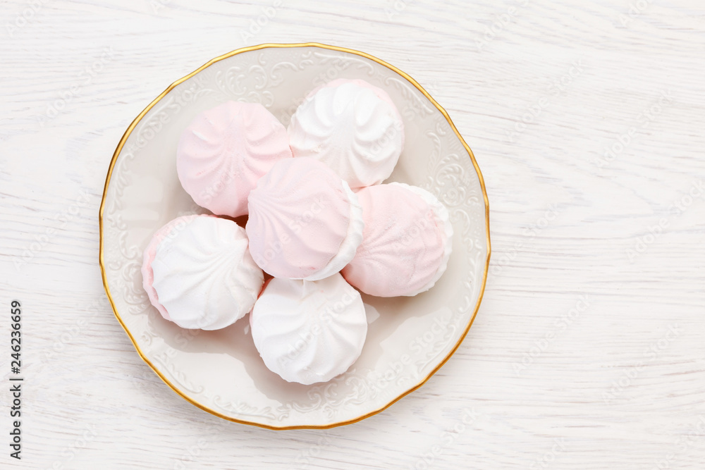 White and pink marshmallow (zephyr) lies on a white plate on a wooden table White and pink marshmallow (zephyr) lies on a white plate on a wooden table