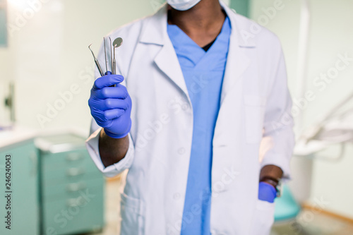 An African American dentist holds mirror and probe in his hands
