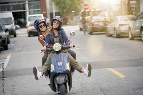 Photos Happy young women riding scooter together in city