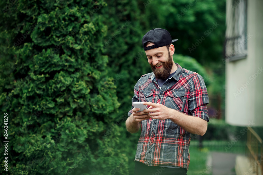 Handsome bearded boy outside using a smartphone. Male with beard in casual outfit reading a message from his phone.