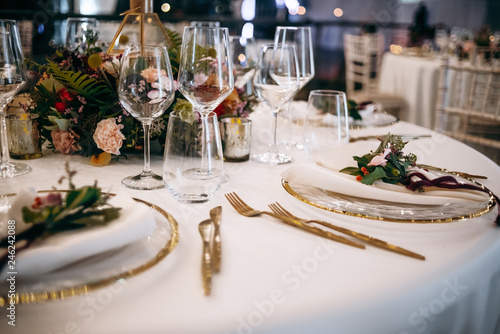 Wedding dinner table setting. White clothes with golden decor and flower bouquets in the center