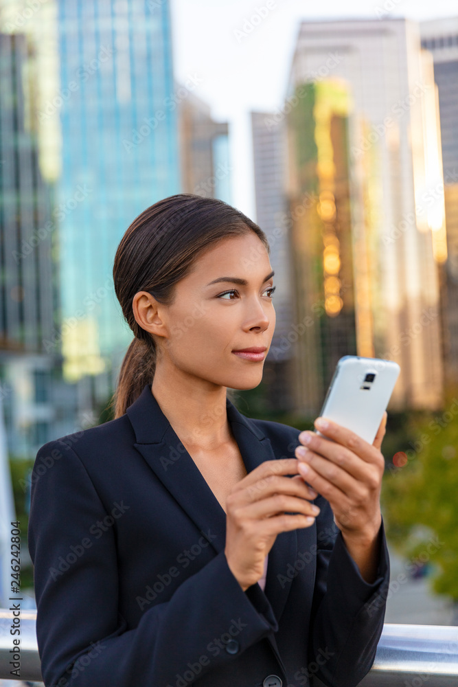 Asian business woman texting on mobile phone looking away to the side city background. Office building outdoors working people. Chinese businesswoman using smartphone with hand. Asian business woman texting on mobile phone looking away to the side city background. Office building outdoors working people. Chinese businesswoman using smartphone with hand.