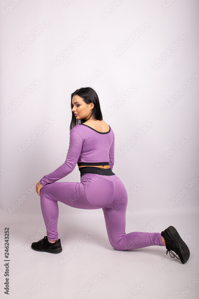 Side profile view portrait of beautiful healthy sporty woman wearing purple  leggings and white top. Isolated on white background Stock Photo