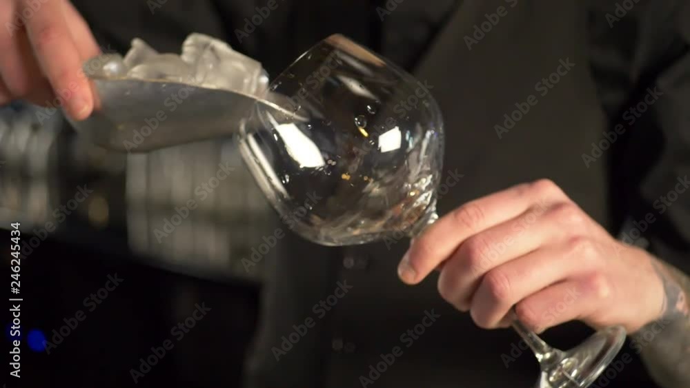 Bartender pour ice cubes into cocktail glass for making fresh alcoholic drink on the bar counter