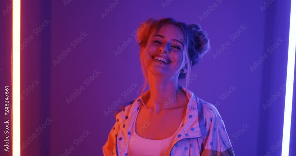 Back view on the blond Caucasian pretty girl turning to the camera and smiling joyfully on the neon lighting background. Rear. Close up. Back view on the blond Caucasian pretty girl turning to the camera and smiling joyfully on the neon lighting background. Rear. Close up.