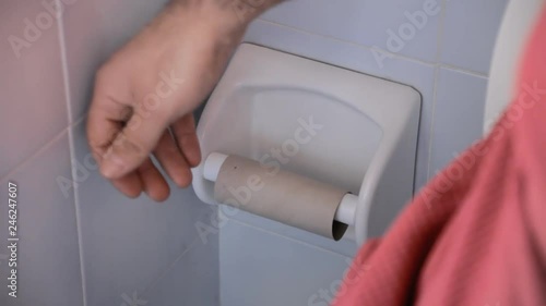 A man in the bathroom, sitting on the toilet, discovering that there's no more paper left on the roll: what a bad surprise.