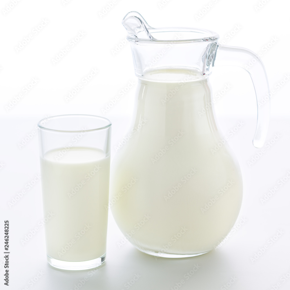 Transparent jug and a glass completely filled with fresh cow milk stand on a clean white background. Transparent jug and a glass completely filled with fresh cow milk stand on a clean white background.