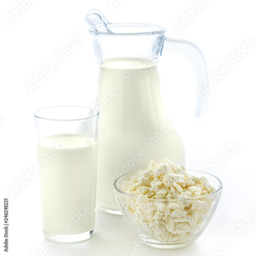 Transparent glass and a jug of useful fresh milk along with a plate of cottage cheese on a clean white background.