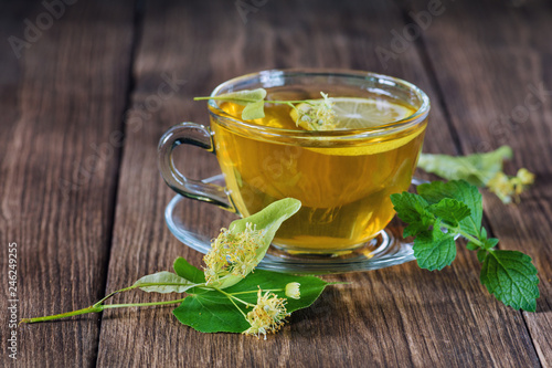 Lime green tea. A cup of tea, standing on a wooden table, surrounded by fragrant linden flowers, in the rays of sunlight.