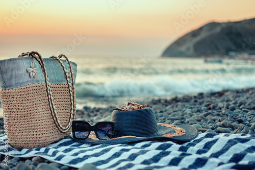 Rest by the sea. Summer women's beach accessories for your sea holiday: straw hat, sunglasses, beach bag and striped towel, seashell.