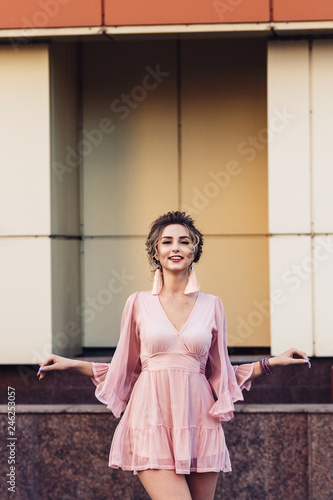 attractive young girl in a short pink dress posing near a beautiful building.