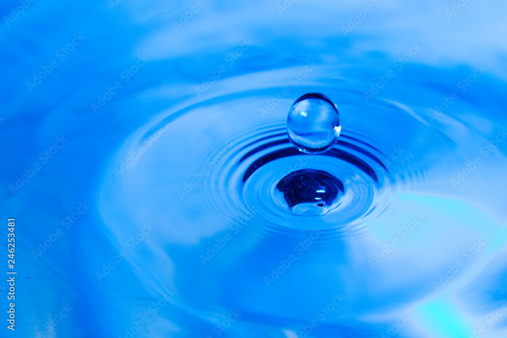 The blue waterdrop falls into the blue water with dispersing circles close up The blue waterdrop falls into the blue water with dispersing circles close up