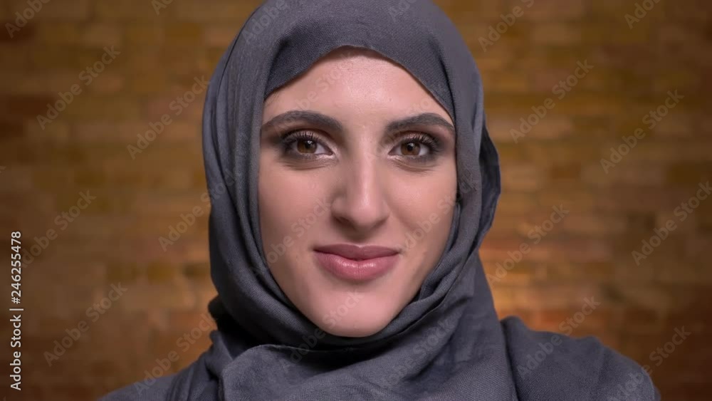 Portrait of beautiful muslim woman in hijab with bright make-up shyly turning her head and smiling into camera on bricken wall background. Portrait of beautiful muslim woman in hijab with bright make-up shyly turning her head and smiling into camera on bricken wall background.