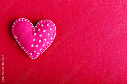 Red heart made of felt on a red background. Handmade blank for greeting card  copy space.