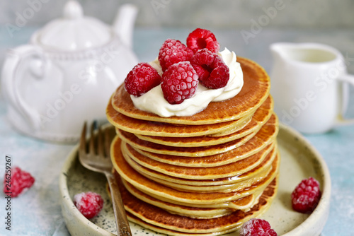 Stack of homemade delicious hot pancakes with honey, cream and raspberry.