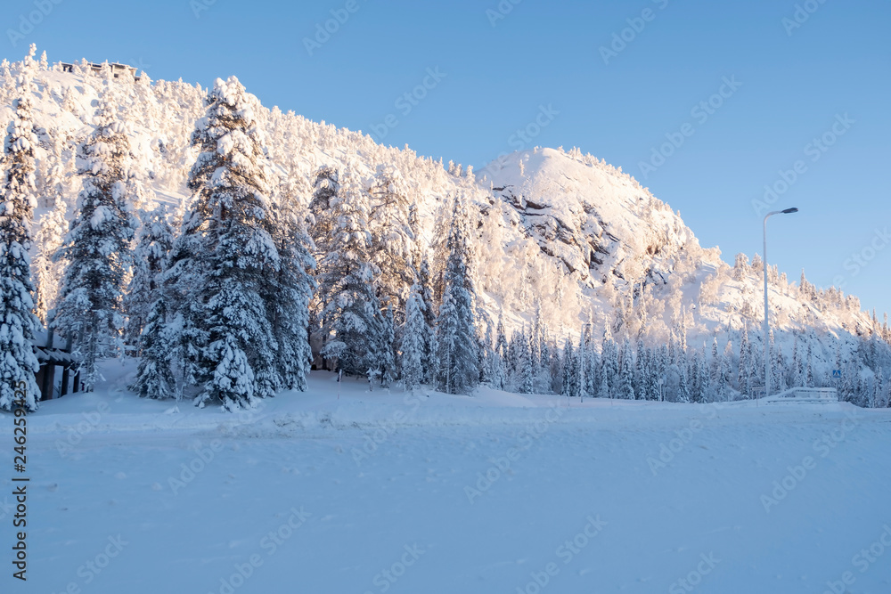 Snow-covered mountain, blue cloudy sky. The top of the mountain is illuminated by sunlight. Lapland Finland, Lapland. Snow-covered mountain, blue cloudy sky. The top of the mountain is illuminated by sunlight. Lapland Finland, Lapland.