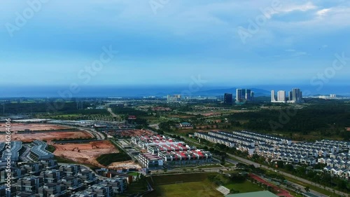 Aerial wide shot of a new construction zone with a lot of new houses in green sorroundings, a street with a car passing by is in on the right side, skyscrapers in the background, Vietnam photo