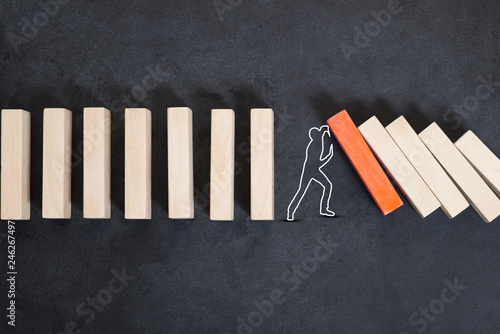 Man silhouette stopping domino effect on dark background or chalkboard photo
