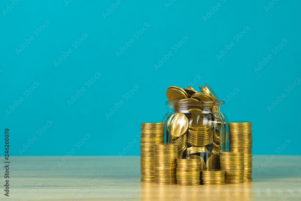 Coins stacks and gold coin money in the glass jar on table with green background, for saving for the future banking finance concept. Coins stacks and gold coin money in the glass jar on table with green background, for saving for the future banking finance concept.