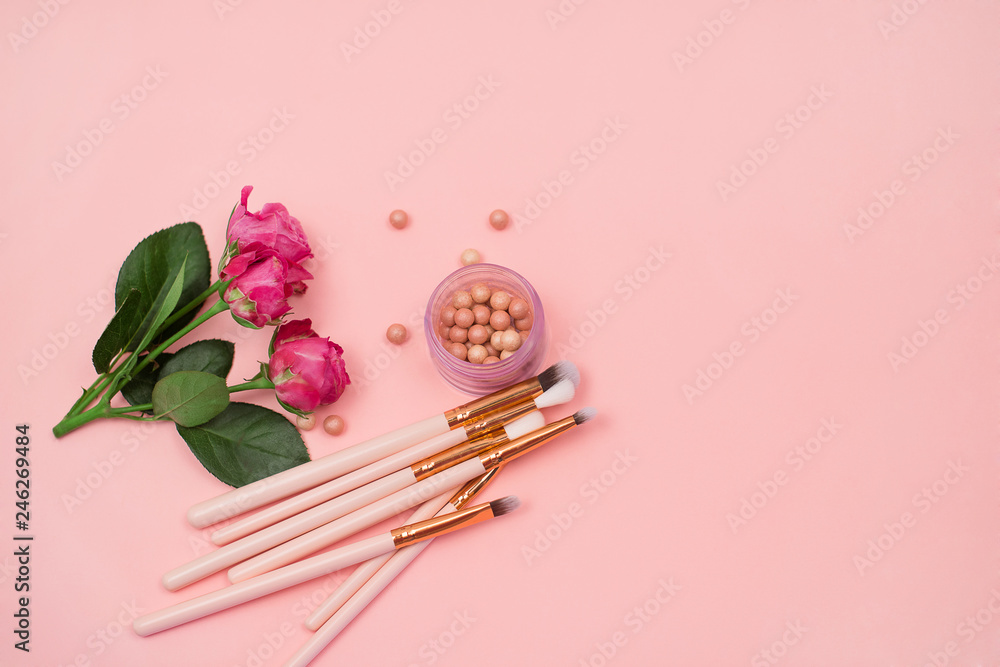  Cosmetics, makeup brushes and flowers on a pink background. Close-up. Top view.