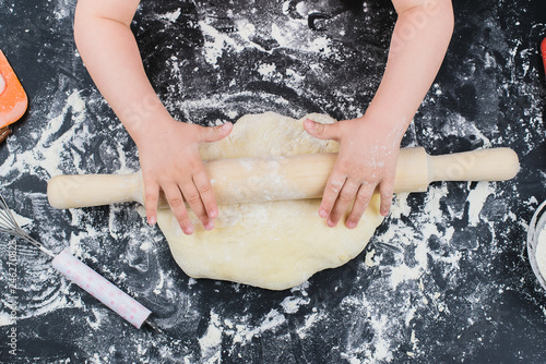 child hands making the dough with flour, rolling pin and wheat ears on rustic wooden table top view. Homemade pastry for bread or pizza. Bakery background. 