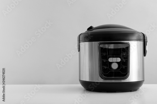 Modern electric multi cooker on table against grey background. Space for text