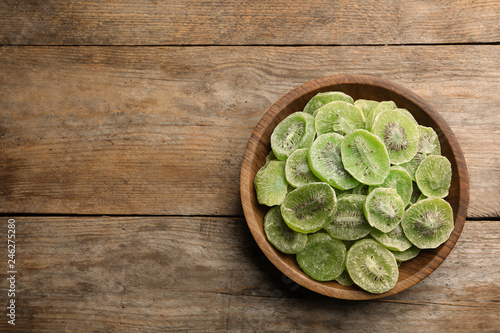 Bowl of dried kiwi on wooden background, top view with space for text. Tasty and healthy fruit