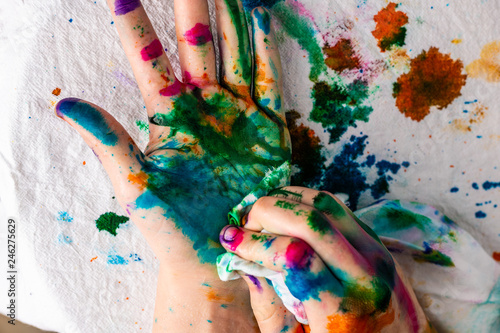  A child cleans up hands that are covered in red, pink, yellow, orange, red, blue, green, and purple ink. Concepts: art, education, play, watercolor, finger painting, mess, creativity, fun, enjoyment