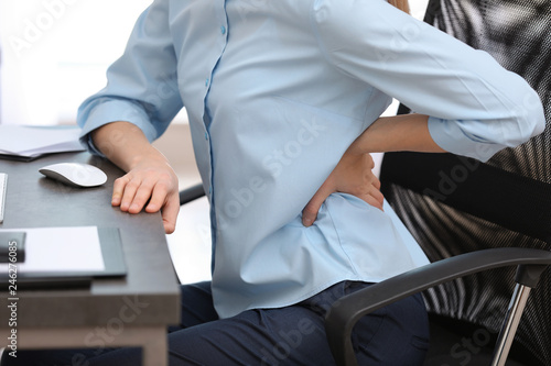 Young woman suffering from back pain in office, closeup